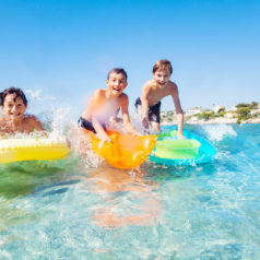 Portrait of three teenage boys, happy friends, surfing the beach waves in summer